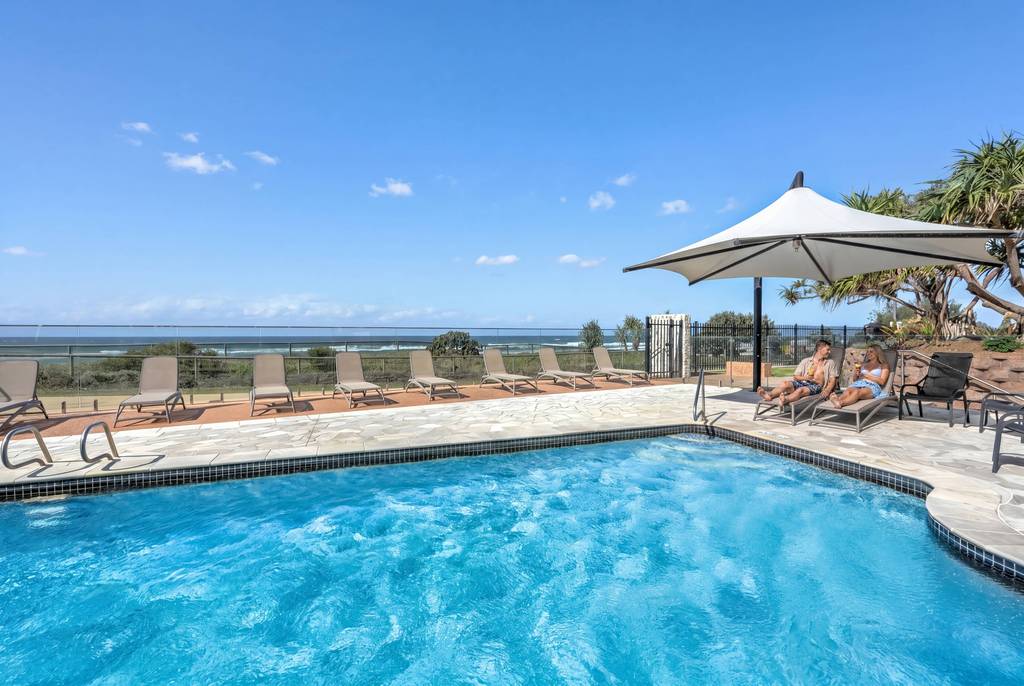Heated outdoor pool surrounded by palm trees and chairs